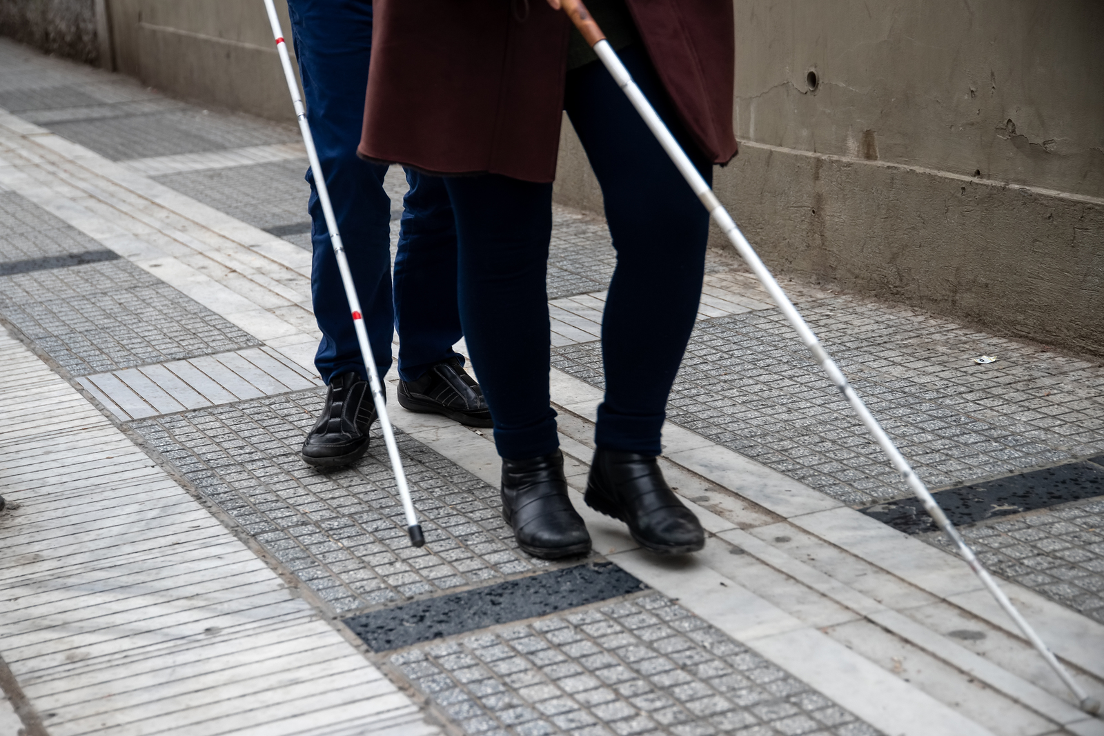 A couple walking down a paved path, with white mobility canes.